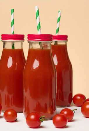 Glass bottles with tomato juice with red caps. Fresh red tomatoes lie on a white tableの写真素材
