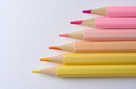 Close-up of six sharp-tipped colored pencils arranged horizontally with color gradation from hot...