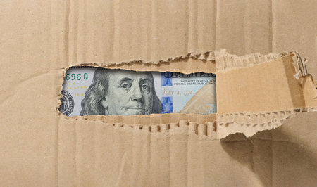 Hundred dollar bill is visible through a hole in the paper. Symbolism of hidden or concealed wealth, money that remains out of sight, or financial resources.の写真素材