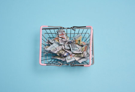 A metal shopping basket with pink handles filled with crumpled dollar bills. The concept of...