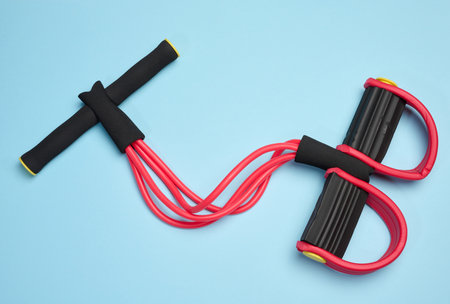 Red and black fitness expander, four elastic tubes, soft handles and foot rests on a blue background