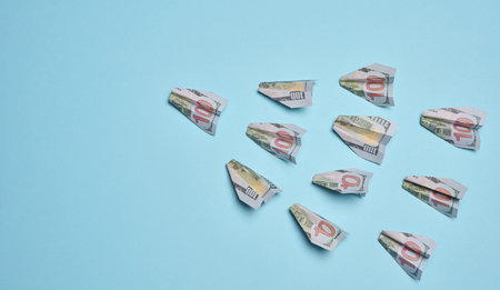 Paper airplanes made of hundred-dollar bills flying in one direction, against a blue background....