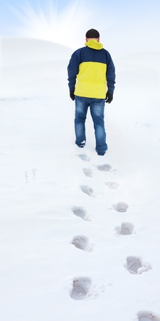 Man in yellow jacket walking on snow, footprints in snow, behindの写真素材