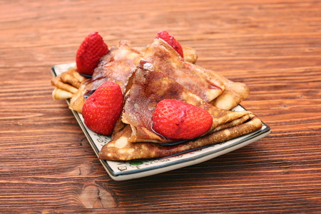 Pancakes with strawberries and syrup on wooden background