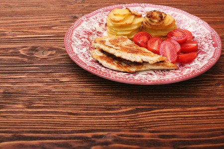 Fried turkey fillets, roasted potatoes and cherry tomato on wooden backgroundの写真素材
