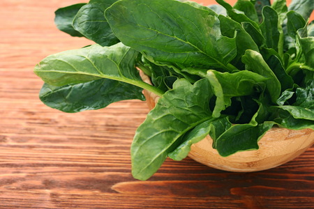 Fresh spinach leaves in bowl on wooden background