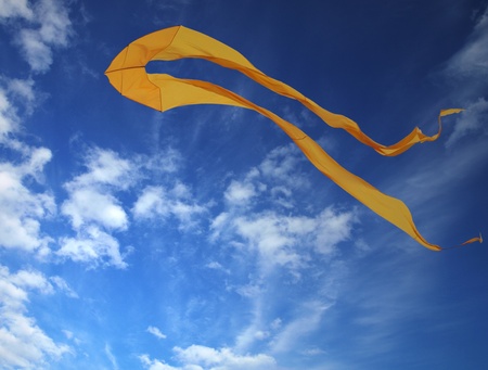 Yellow kite soaring in blue sky       の写真素材