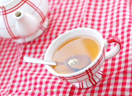 A cup of tea and a teapot on a red checked clothの写真素材