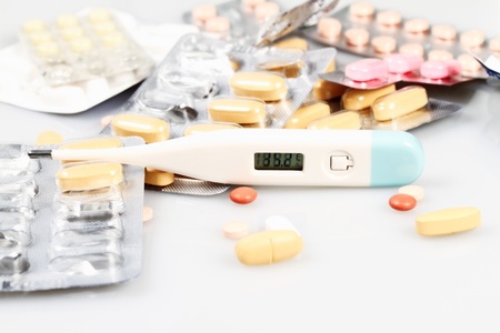 Yellow pills and thermometer on a white background