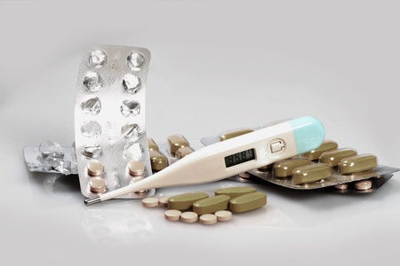 White pills and thermometer on a white background
