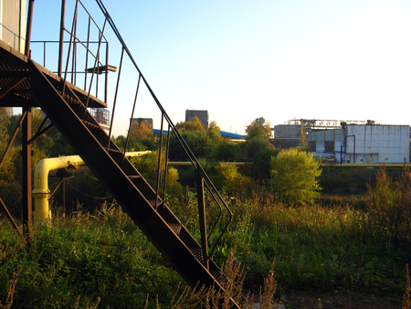 Iron staircase and part of the pipeline against the background of factory buildingsの写真素材