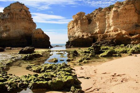 Rocks on the Praia de SÃ£o Rafael beach, Algarve, Portugal. Lime-gold cliff, green stones with algae on low tide. Beautiful and colorful picture.の写真素材