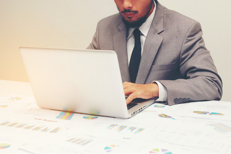 Young man working with laptop, man's hands on notebook computer, business person at workplace over business report papers,data,statisticの写真素材