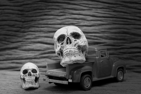 black and white shot of Still life painting photography with human skull on vintage image of pickup truck toy on wooden background.の写真素材