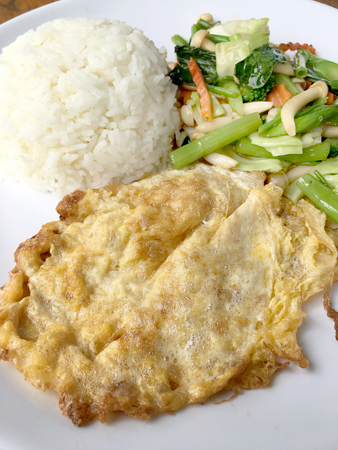 stir fried vegetables with Thai Omelette (scrambled eggs) with rice in white plate on rustic wooden background. Vegetarian Food, healthy food.の写真素材