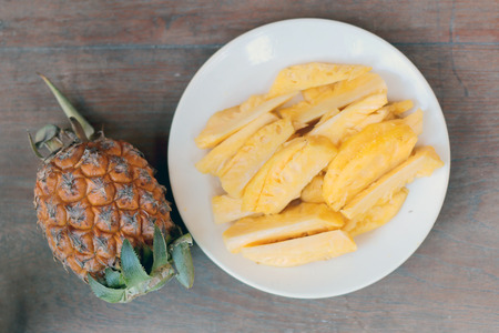 Cutting fresh pineapple and pineapple shelled Asian-style in white dish on the old wooden background. Tropical fruit concept.の写真素材