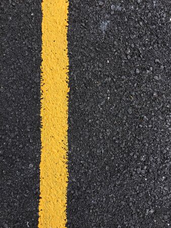 Yellow paint line on black asphalt road surface texture. space transportation backgroundの写真素材