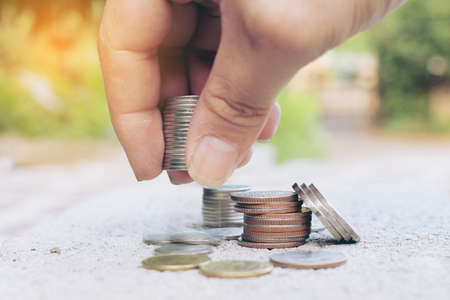 Man's hand put money coins to stack of coins over blurred image of green nature abstract background...