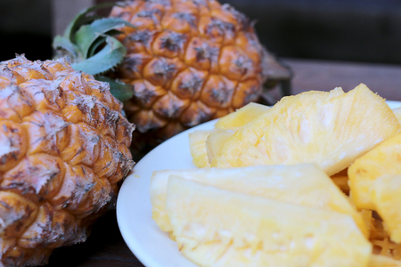 Cutting fresh pineapple and pineapple shelled Asian-style in white dish on the old wooden background. Tropical fruit concept.の写真素材