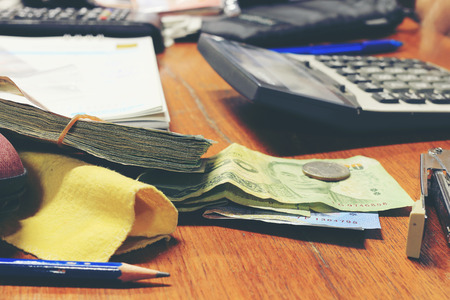 Calculator and money thai banknote with  white notebook paper, pen on wooden table at home office. The concept of financial planning, savings. vintage tone colour and motion blur moving of hand.の写真素材