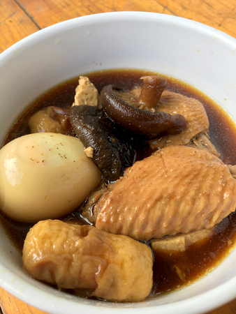Stewed Pork with herb, egg and wing chicken  in Soy Sauce or sweet brown gravy (Moo Pa-lo) in white blow on wooden table,Thai traditional food.の写真素材