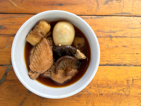 Stewed Pork with herb, egg and wing chicken  in Soy Sauce or sweet brown gravy (Moo Pa-lo) in white blow on wooden table,Thai traditional food.の写真素材
