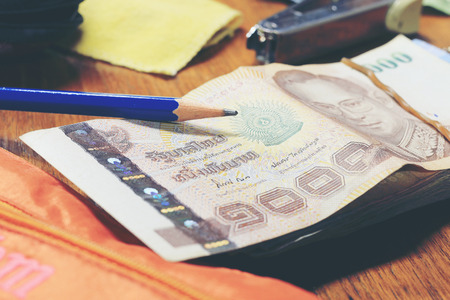 Calculator and money thai banknote with  white notebook paper, pen on wooden table at home office....