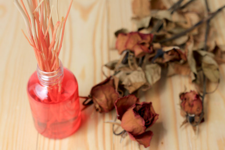 Hand made pf Fragrance Diffuser Set: bottle with aroma sticks and dry red rose (reed diffusers), a spray bottle with perfume on pine wood table with wall background.の写真素材