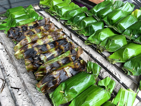 Thai traditional desserts, Thailand dessert wrapped in banana leaves, coconut milk custard with coconut sweet on the stove for cooking, Thai grilled sticky rice on a grilled, street foodの写真素材