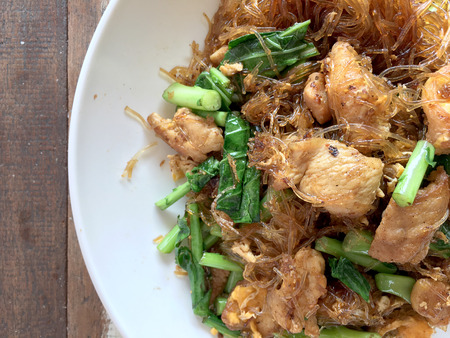 Stir fried Flat Rice Noodle with Soy Sauce and Pork in white dish on colourful wooden table in thai called "Pad See Eww". Thai style food.の写真素材