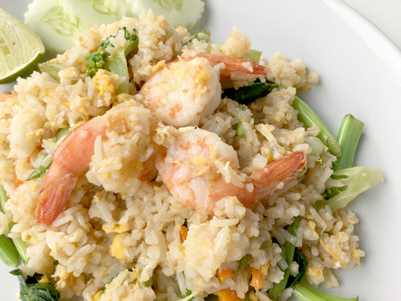 Fried rice with prawn herbs and vegetables served with lemon and cucumber in white plate on white background. Part of a series of nine Asian food dishes. Thai Food.の写真素材