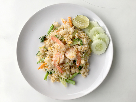 Fried rice with prawn herbs and vegetables served with lemon and cucumber in white plate on white background. Part of a series of nine Asian food dishes. Thai Food.の写真素材