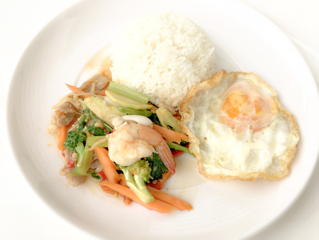 Fried Savory sauteed mixed vegetables with shimp and fried egg served with rice in white dish on white background as Thai homemade meal or recipe in the restaurant. Thai style food.の写真素材