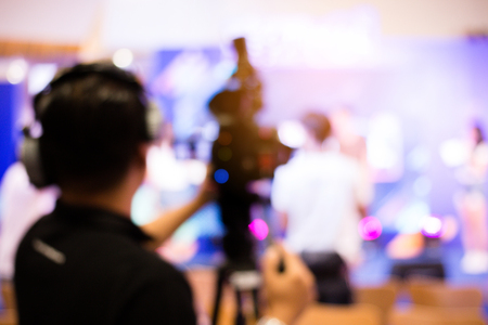 blurred image of young cameraman using a professional camcorder in door at event filming music show...