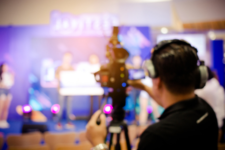 blurred image of young cameraman using a professional camcorder in door at event filming music show or mini concert for shooting some video movie and live broadcasting for online TV commercialの写真素材