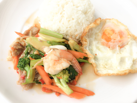 Fried Savory sauteed mixed vegetables with shimp and fried egg served with rice in white dish on white background as Thai homemade meal or recipe in the restaurant. Thai style food.の写真素材