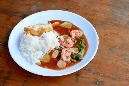 stir fried shrimp and Broccoli in thai red curry paste sauce with rice, Curry fried shrimps and cooked rice in white dish closeup on wooden table. Thai style food.の写真素材