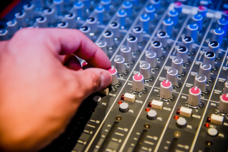 close-up hands of sound engineer adjusting audio mixer controller for live music and studio equipment. This is a quality audio system for professionals. vintage tone & effect light in control room.の写真素材