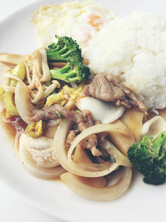 Thai cuisine. Stir-fried colorful vegetables, onion, broccoli, mushroom with meat in white plate with rice and fried egg on white background. Thai style food in fast street restaurant.の写真素材