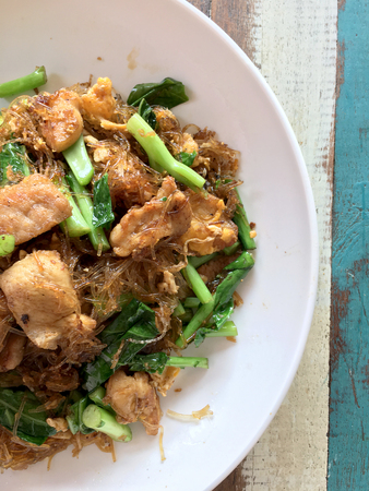 Stir fried Flat Rice Noodle with Soy Sauce and Pork in white dish on colourful wooden table in thai called "Pad See Eww". Thai style food.の写真素材