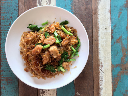 Stir fried Flat Rice Noodle with Soy Sauce and Pork in white dish on colourful wooden table in thai called "Pad See Eww". Thai style food.の写真素材