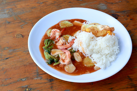 stir fried shrimp and Broccoli in thai red curry paste sauce with rice, Curry fried shrimps and cooked rice in white dish closeup on wooden table. Thai style food.の写真素材