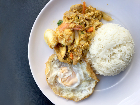 Stir fry prawns and squid with curry power thai style with fried egg with rice in white dish on black fabric texture background. Thai style food.の写真素材