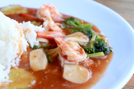 stir fried shrimp and Broccoli in thai red curry paste sauce with rice, Curry fried shrimps and cooked rice in white dish closeup on wooden table. Thai style food.の写真素材