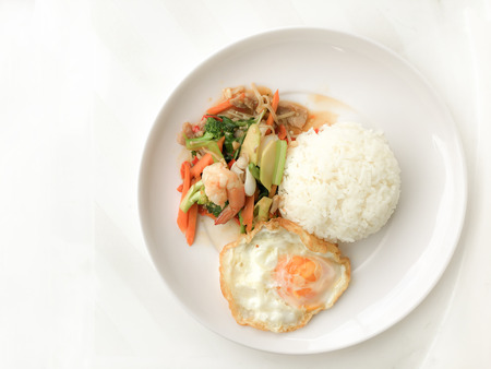 Fried Savory sauteed mixed vegetables with shimp and fried egg served with rice in white dish on white background as Thai homemade meal or recipe in the restaurant. Thai style food.の写真素材