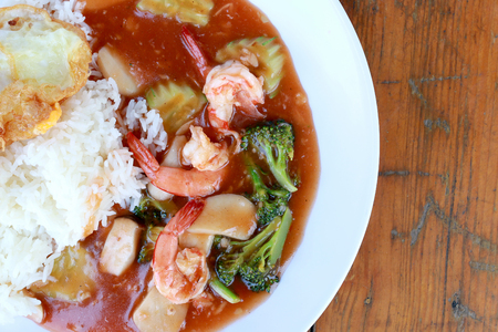 stir fried shrimp and Broccoli in thai red curry paste sauce with rice, Curry fried shrimps and cooked rice in white dish closeup on wooden table. Thai style food.の写真素材