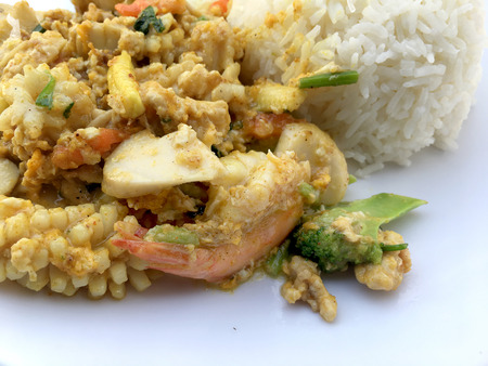 Stir-fried seafood, prawn and squid with yellow curry powder with rice and fried egg in white plate on white background. Thai style food.の写真素材