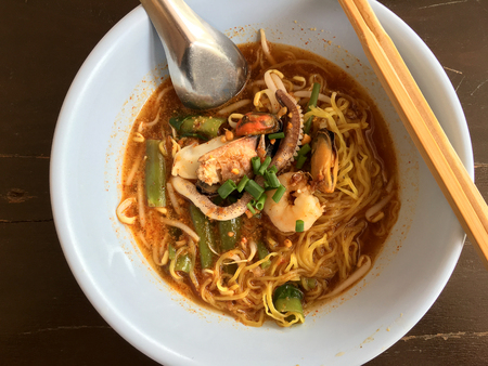 Delicious asian spicy seafood noodle soup with shrimp, squid and shellfish in white bowl on wooden table, Tom Yum Goong. Thai style food. vintage tone color filter.の写真素材