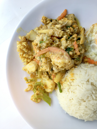 Stir-fried seafood, prawn and squid with yellow curry powder with rice and fried egg in white plate on white background. Thai style food.の写真素材
