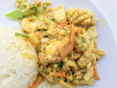 Stir-fried seafood, prawn and squid with yellow curry powder with rice and fried egg in white plate on white background. Thai style food.の写真素材